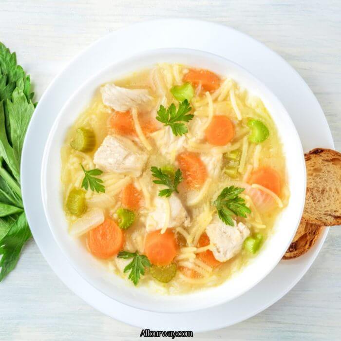Rich chicken broth with chunks of chicken, carrots, celery noodles and parsley leaves on top.