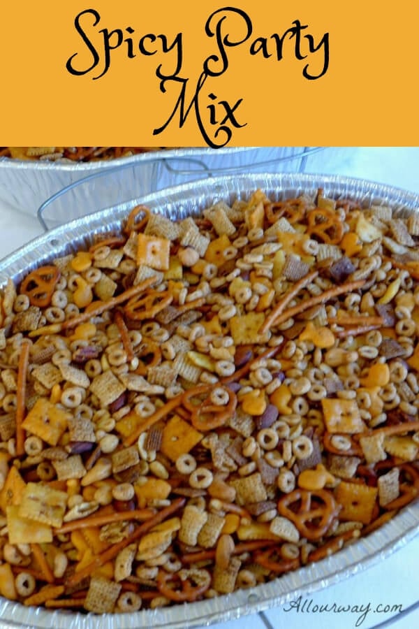 A large aluminum roasting pan filled with party mix consisting of nuts, Chex cereal, pretzels, Cheerios, and square crackers, 