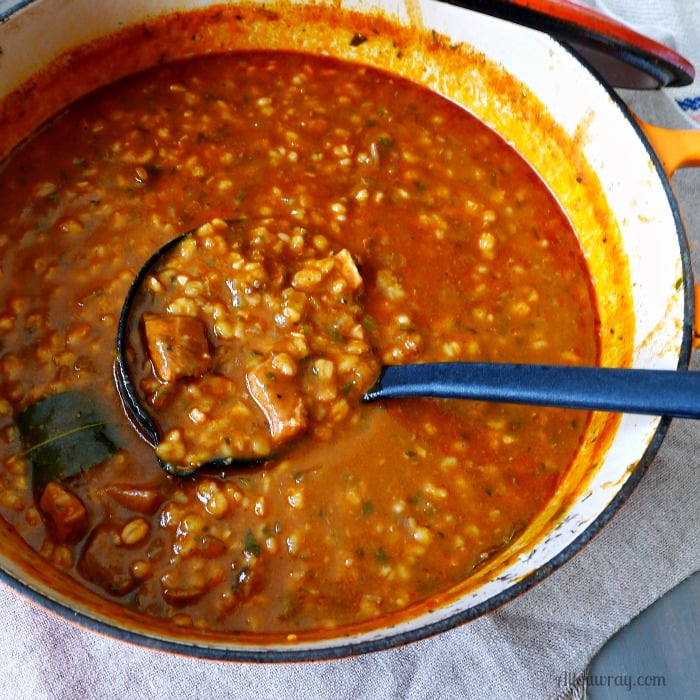 White porcelain lined pot filled Beef Barley Soup and a black ladle ready to scoop up a portion. 