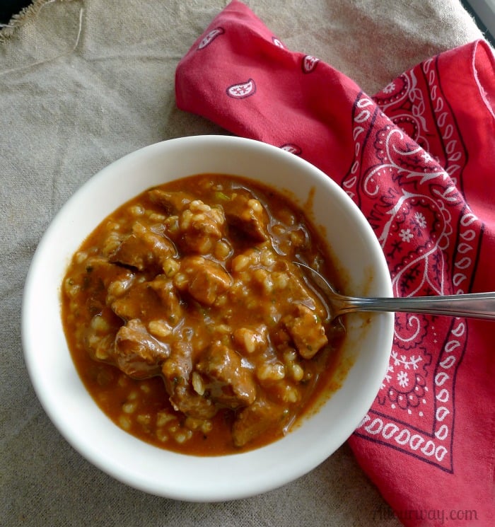 A white bowlful of red Soup with a spoon in the rich broth. A red bandana on the side acts as a napkin.
