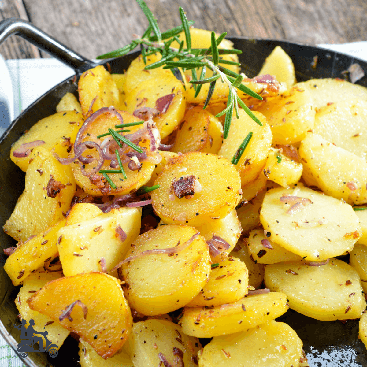 Skillet full of sliced potatoes that are fried and sprinkled with herbs. 