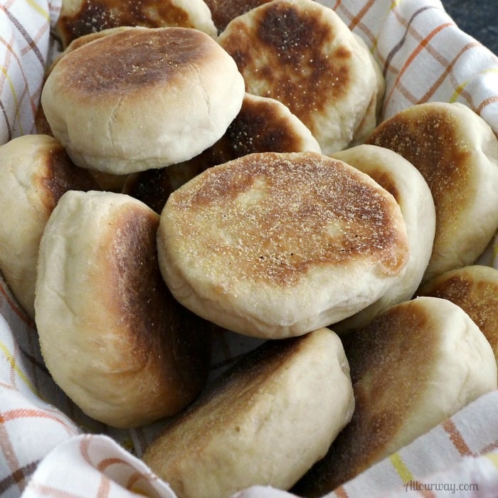 English Muffins piled on a brown orange yellow plaid towel lined bread basket.