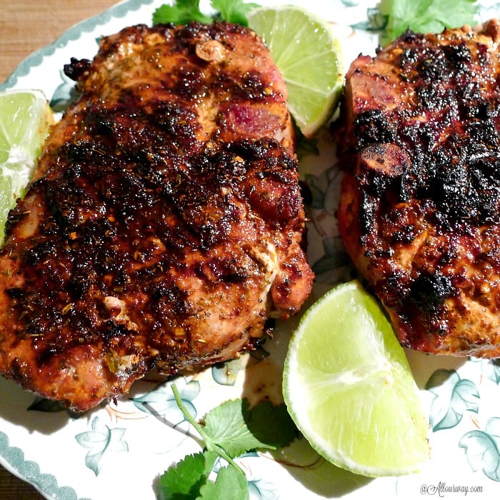 Close up of two Grilled Lime Adobo Rubbed Pork Chops with cilantro and lime wedges surrounding the meat all on a white and green leaf china platter. 