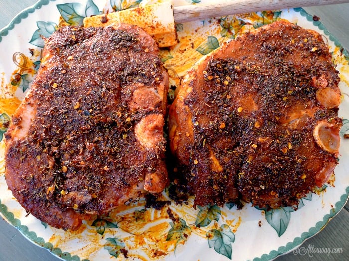 Two paprika and lime rubbed bone-in pork chops on a white and green leaf platter with a yellow spatula on the plate. 