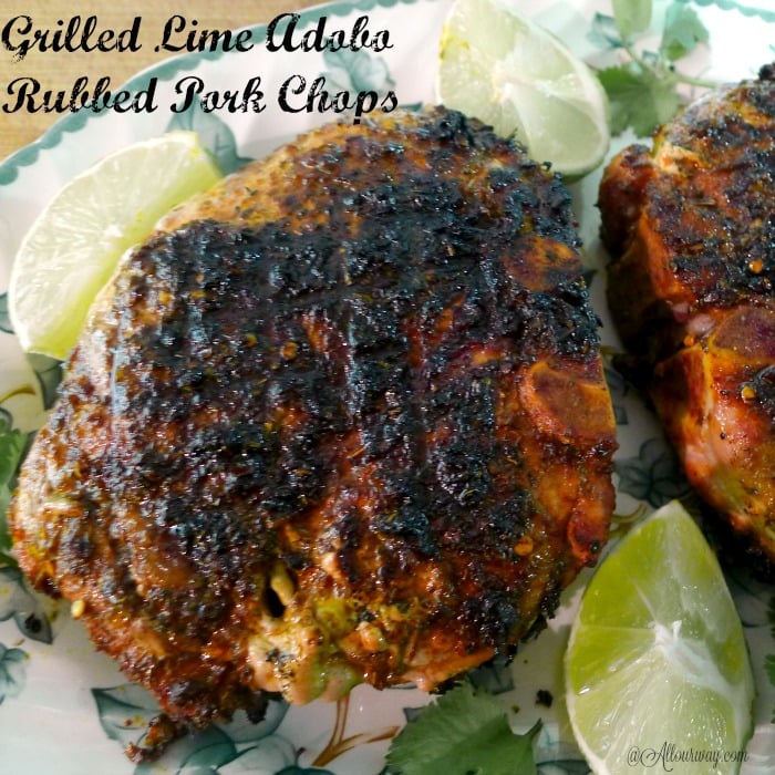 Close up of the beautifully browned grilled pork chops on a green leaf and white plate with lime wedges and green cilantro around the chops.