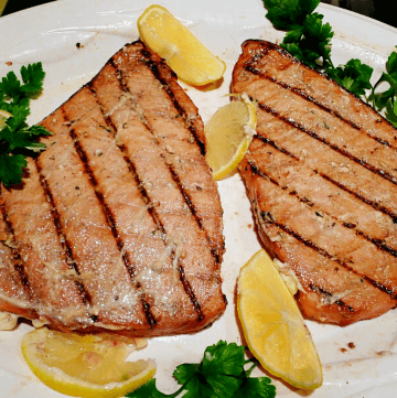 Swordfish with grill marks on white plate with lemon wedges and parsley