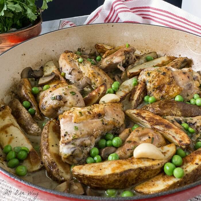 Chicken Vesuvio with Mushrooms and green peas in a white porcelain lined red pan with a white and red striped dishtowel along side.