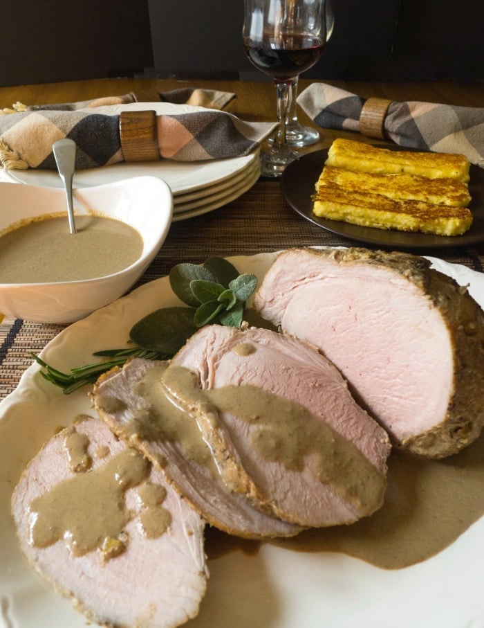 Italian Roast Pork Braised in Milk with Fresh Herbs sliced on white platter with gravy by its side