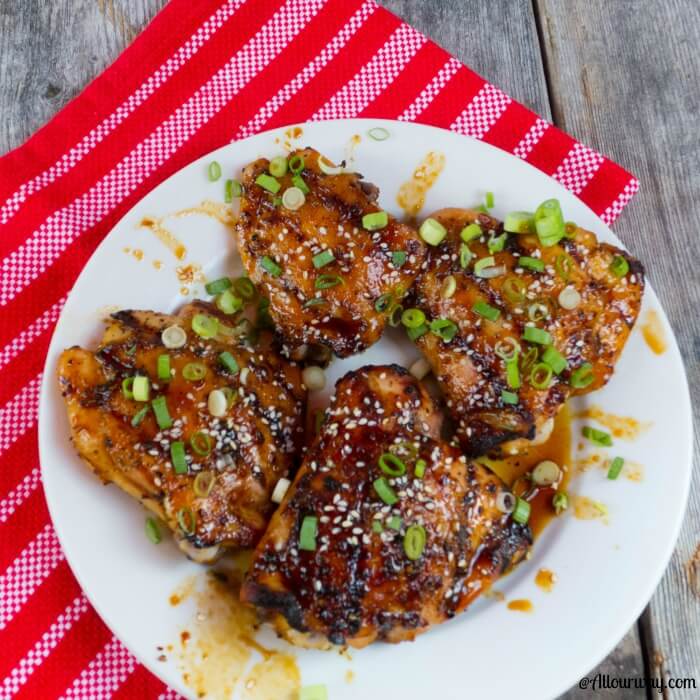 Four Amazing Blazing Asian Grilled Chicken Thighs on white plate with a red and white striped tea towel in the backround.