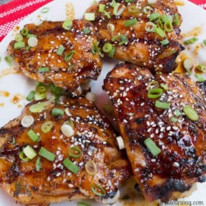 Four Amazing Blazing Asian Grilled Chicken Thighs on white plate with a red and white striped tea towel in the background.