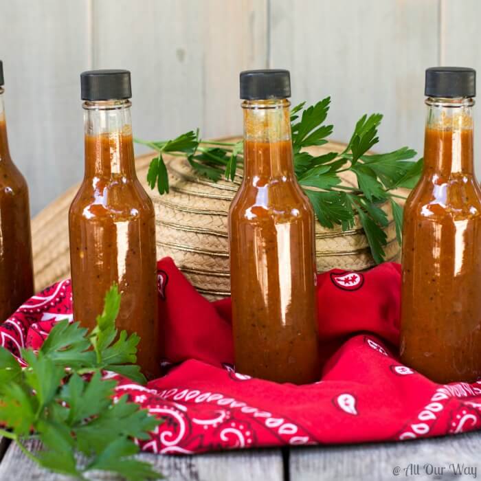 Close up of three small hot sauce bottles sitting on a red bandana, straw hat, and two sprigs of green parsley.i