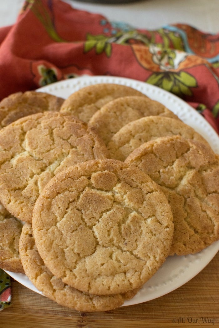 Brown Butter Snickerdoodle Cookies stacked on a white plate on a wood cutting board and a russet napkin below the plate.