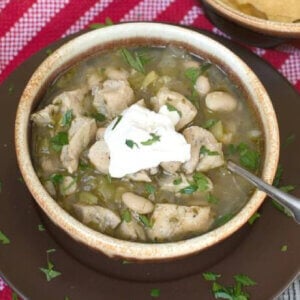 Wickedly Good Spicy White Chicken Chili with Lime and Cilantro in a brown earthenware bowl with a spoon.