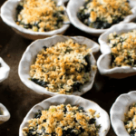 Black Tray with Oysters Rockefeller in white porcelain half shells.
