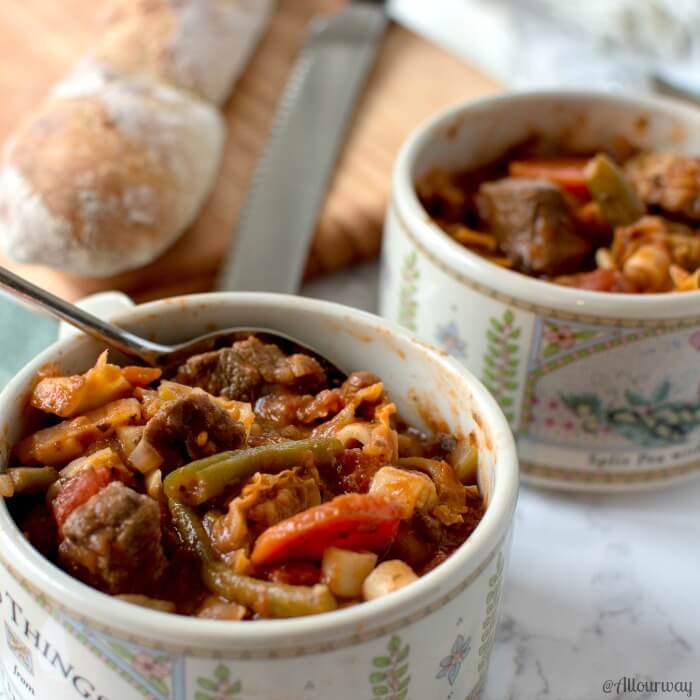 Two Rustic Italian Vegetable Beef Stew Ready in white bowls with a spoon in one bowl. A baguette is on a wood board with a knife. @allourway.com