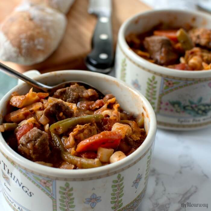 Two bowls of Rustic Italian Vegetable Beef Stew with a loaf of bread on a wooden cutting board and a knife on the side. 