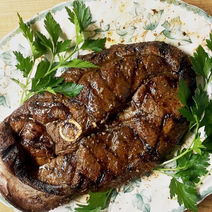 Venison steak resting on a white a green leafed plate with green parsley on either side. 