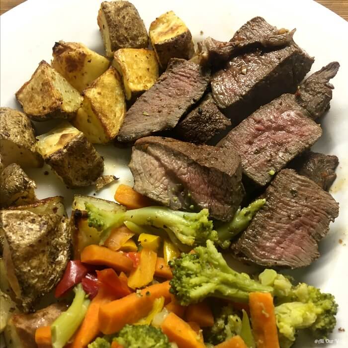 Venison steak dinner with browned potato chunks and a melange of vegetables comprising of broccoli, carrots, and red peppers. 
