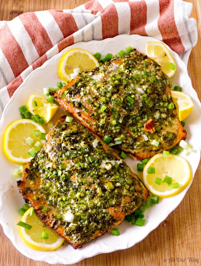 Grilled Italian Pesto Salmon on white oblong platter with lemon slices surrounding the fish, the platter on burgundy stripped dish towel.