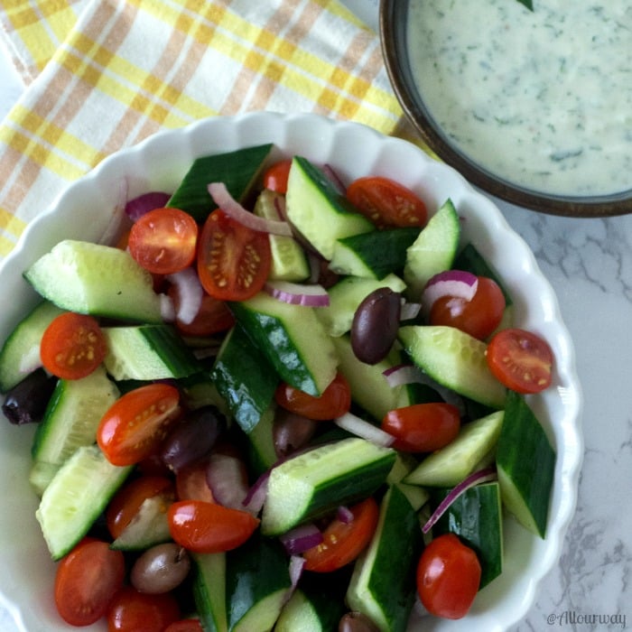 Mediterranean Tomato Cucumber Salad with Spicy Yogurt Dressing in a big white bowl with a yellow and white tea towel next to it. @ allourway.com