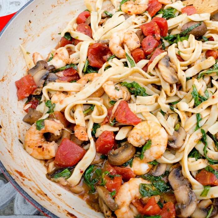 Shrimp stir fry Italian Style with arugula and tomato bits in an enameled lined cast iron red braiser.