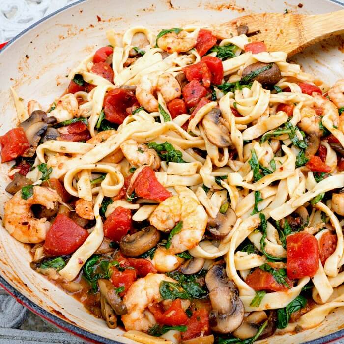 Shrimp Stir Fry Italian Style with pasta, tomatoes, arugula in a large enameled braiser. 