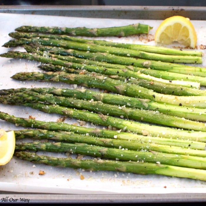Roasted Lemon Garlic Asparagus with Parmesan on a parchment lined baking sheet with lemon wedges and sprinkles of salt and parmesan. 