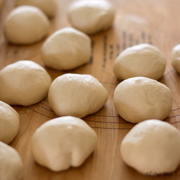 Balls of dough on a wooden bread board ready to be made into rounds. 