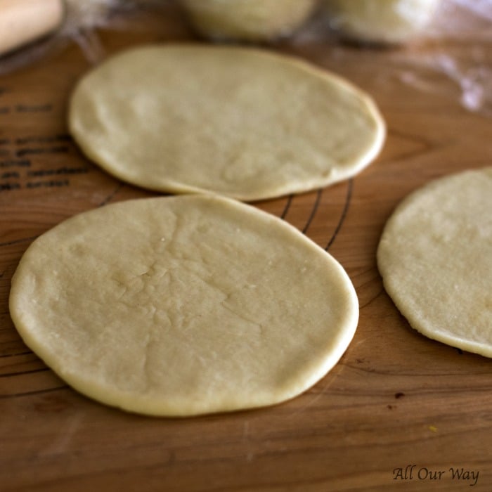 Yeast dough is flattened into rounds on top of wooden bread board. 