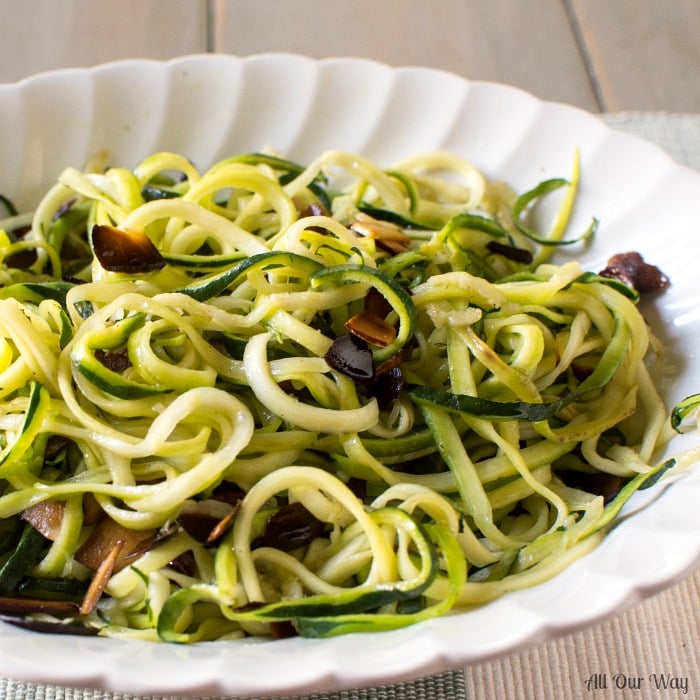 Close up of Zucchini Noodles and sautèed almonds in a white fluted oblong china bowl.