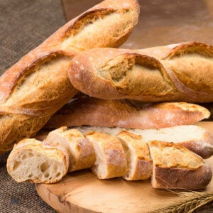 Baked baguettes on table with sliced loaf on wood cutting board.