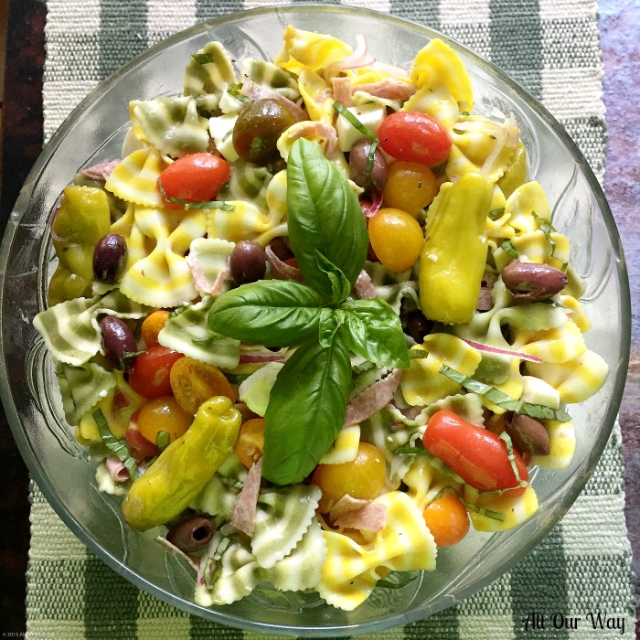 Lemon Basil Farfalle Salad in a glass bowl. A combination of striped bow pasta, grape tomatoes, hot peppers, black olives, mozzarella cubes