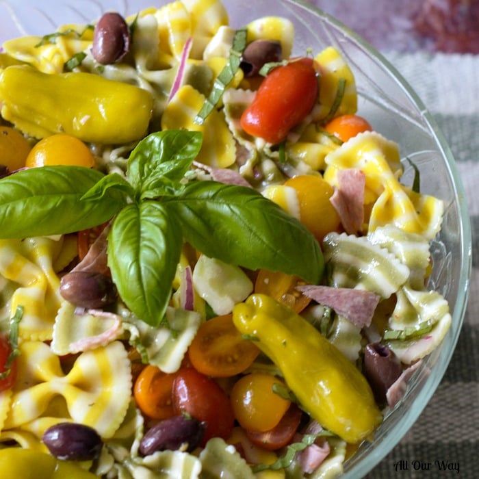 Italian Pasta Salad with striped yellow and green pasta in a glass bowl with tomatoes, black olives, peperoncini. 