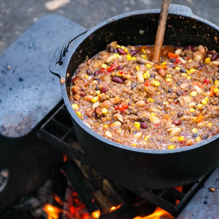 Big cast iron pot over an open fire with Hearty Venison Chili is a modern creation from the Chili con Carne at a campfire. 