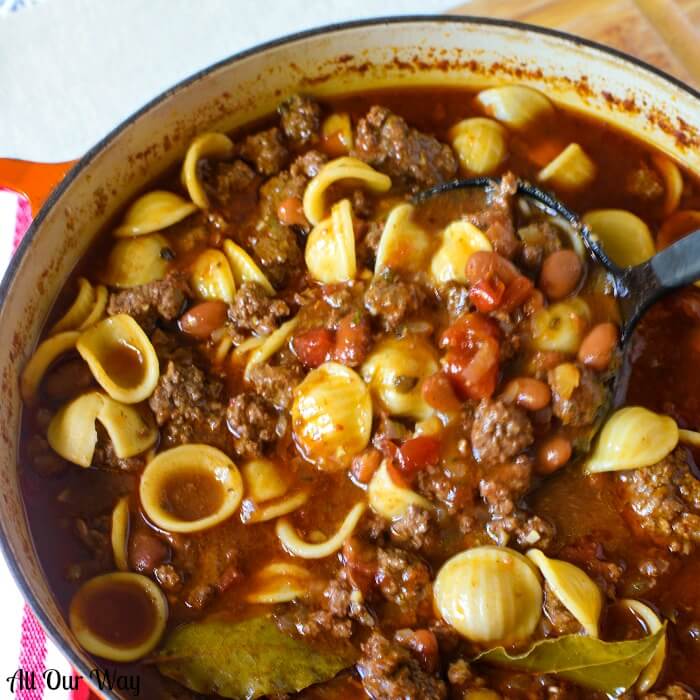 Hearty Venison Chili is slow-cooked and full of flavor in a large red Dutch oven. Chunks of meat, beans and pasta are in the large pot. 