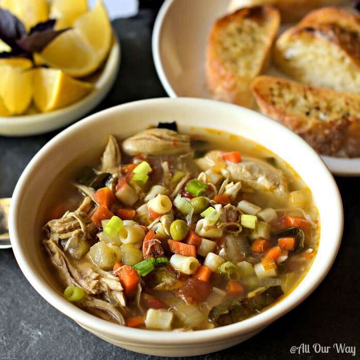 chicken soup in bowl, pasta in soup, lemon wedges, bread for dunking, roasted chicken vegetable soup