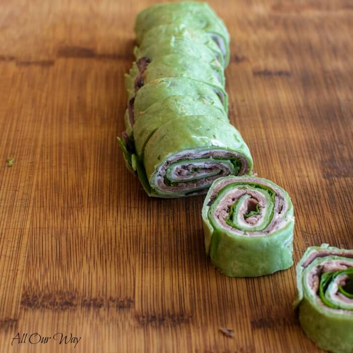 Tortilla pinwheels recipes show Spinach tortilla log sliced in spirals and on bamboo cutting board. 