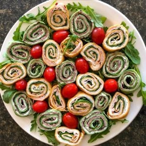 appetizer pinwheels on a white plate with grape tomatoes and a bed of arugula.