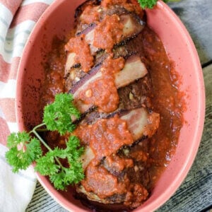 Polpettone Italian Stuffed Meatloaf in red casserole dish with green parsley on the side. Sits on top of a gray wood table and a red striped dishcloth.