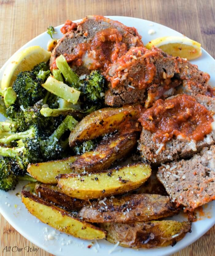 Polpettone Italian stuffed meatloaf on white plate with broccoli, wedged baked potatoes and slivers of lemon. 