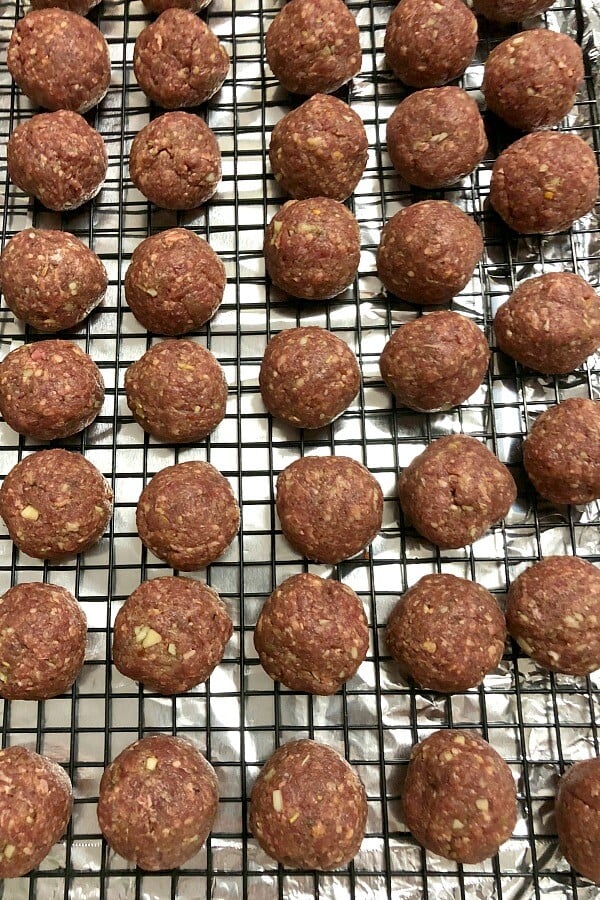 Rows of baked venison meatballs on top of a black wire rack over a foil-lined tray.