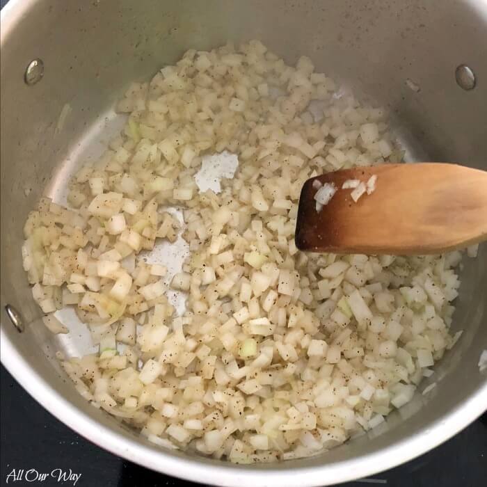 Wooden spoon stirring the onions and garlic in a large pot. 