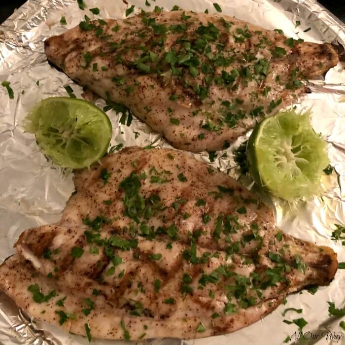 Two Grilled Florida Pompano Fillets on aluminum foiled line baking sheet with 2 lime halves.