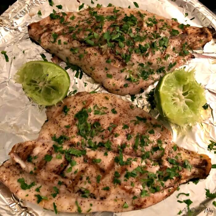 Two Florida Pompano fillets that are grilled on a tray, seasoned with lime and parsley.