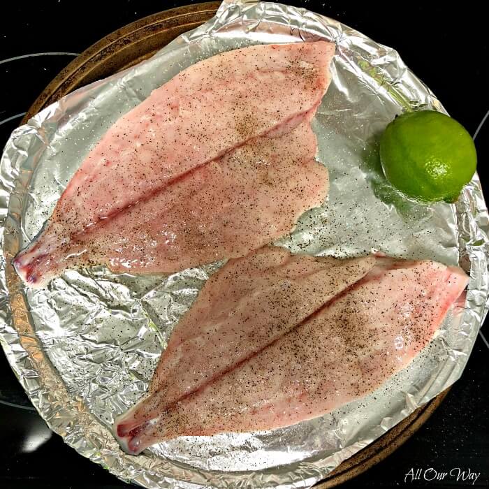 Two Florida Pompano fillets with a lime on a foil lined round baking pan. 