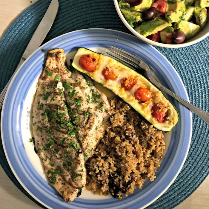 Florida Pompano on a blue rimmed plate with zucchini boats stuffed with tomatoes and quinoa with muchrooms. A salad on the side. 