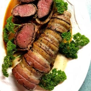 Bacon-wrapped antelope tenderloin with several slices on a white plate with parsley.