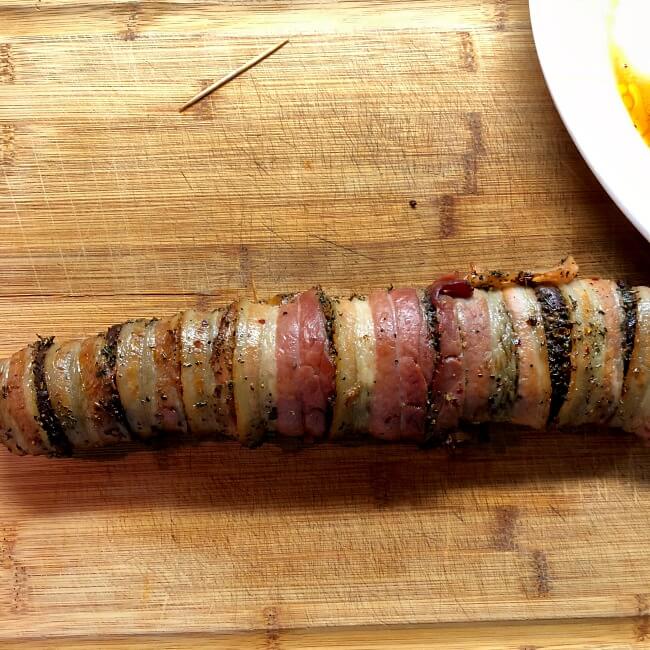 Grilled antelope tenderloin is bacon-wrapped and on cutting board resting before slicing. 