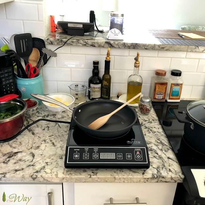 Ingredients for the spinach tortellini and an induction burner with black pan with spoon. 