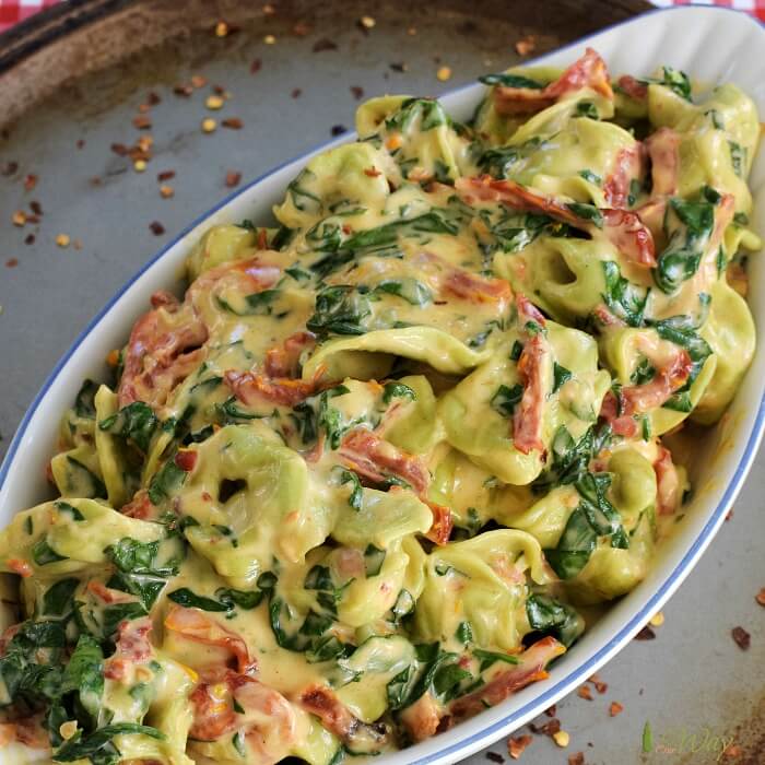 Spinach Tortellini with sun-dried tomatoes and spinach in a gratin dish that sits on a metal tray. 